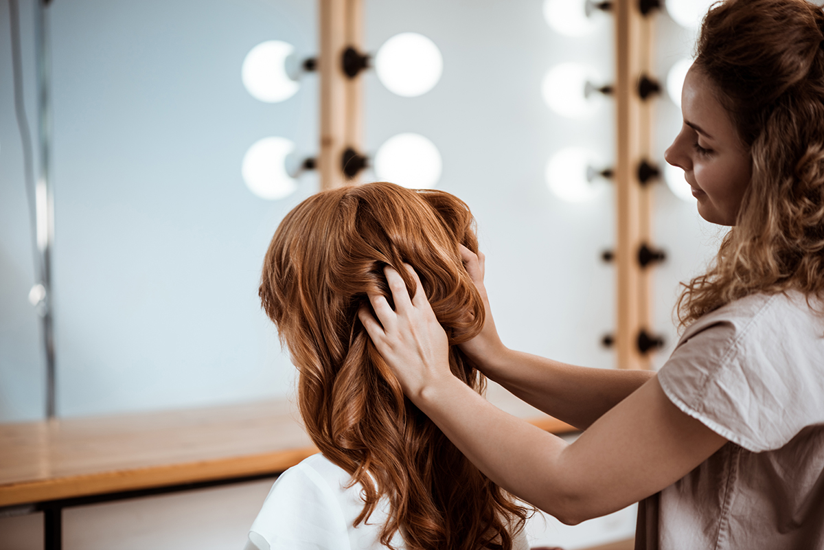 Female hairdresser making hairstyle to redhead girl in beauty salon.